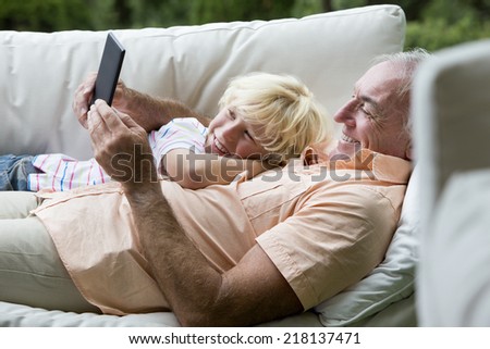 Smiling grandfather and grandson laying on outdoor sofa with digital tablet