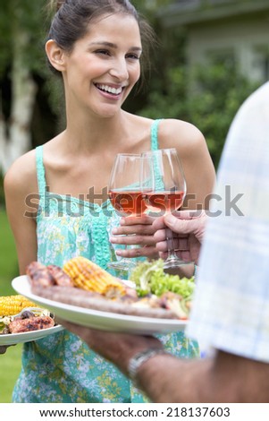 Smiling father and daughter holding plates of barbecue and toasting wine glasses