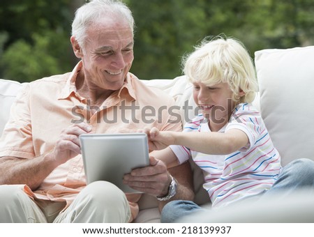 Grandfather and grandson using digital tablet on outdoor sofa