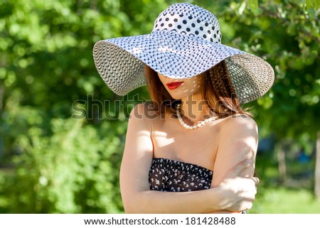 Young woman wearing summer hat and peal necklace. Beautiful brunette in summer garden