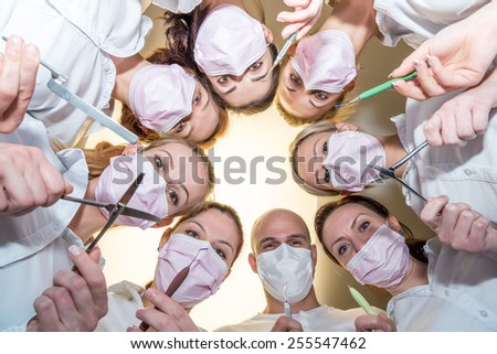 A team of dentists with tools and masks bending over patient