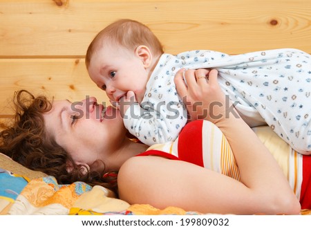 mother hold in hand and kiss son on cover patchwork near wooden wall