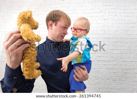 Young dad shows teddy bear to his one year old son on brick background