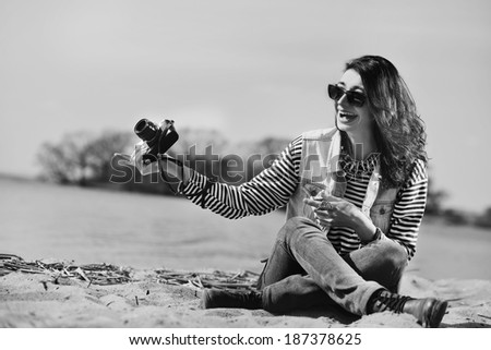 Black and white portrait of a happy laughing girl with camera on the beach sitting on the sand