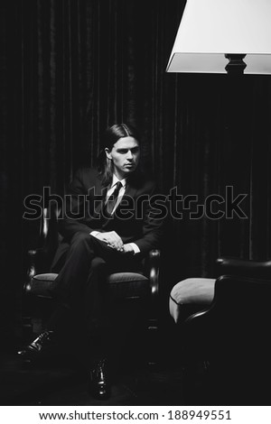 black and white portrait of a man in a suit sitting in a club chair