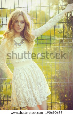 portrait of a beautiful girl in a dress in the sun on the background of the fence outdoor
