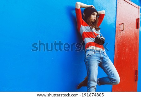 portrait of a beautiful girl with a camera resting on a red wall and blue door
