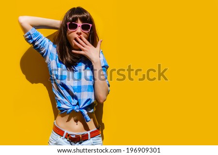 portrait of a beautiful surprised girl in blue shirt and glasses on a background of orange wall