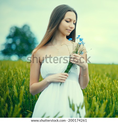 portrait of young woman standing on a wheat field with sunrise on the background outdoor
