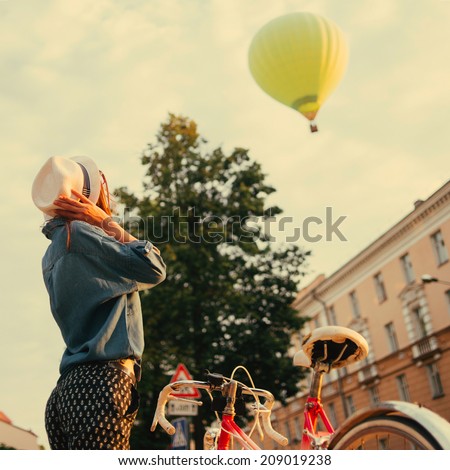 portrait of a beautiful girl with a bicycle in a hat looking at flying the balloon in the city