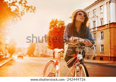 portrait of a beautiful young girl in a hat with a bicycle on city background in the sunlight outdoor