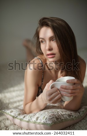 sensual portrait of a beautiful girl with white mug in hand lying on the white carpet in the early morning