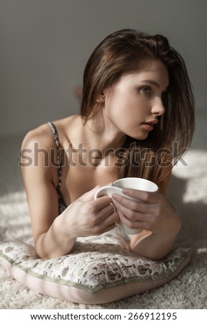 sensual portrait of a beautiful girl with white mug in hand lying on the white carpet