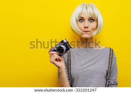 Portrait of a surprise girl with a camera in hand on a yellow background. Isolated studio. Blonde girl.