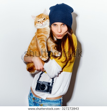 Portrait of a happy crazy hipster girl with camera and ginger cat in a yellow baize and jeans on white background. Retro camera. Hipster girl