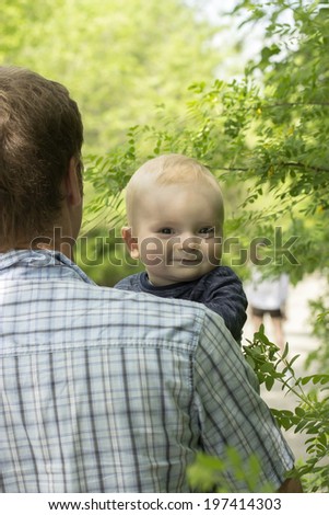 father carrying his smiling baby boy on a walk in the shadow of trees