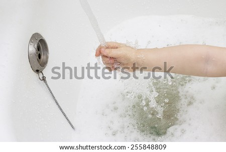 child\'s hand reaching out for a water spray in a bath with foam