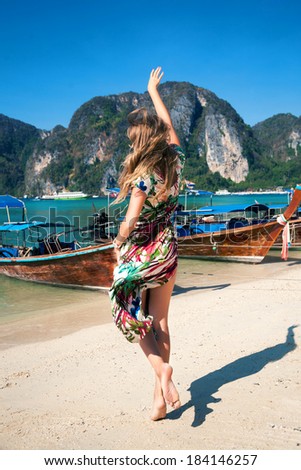 Blonde girl in stylish long colorful tropical print dress jumping and enjoy the moment at amazing koh phi phi. Summer paradise.