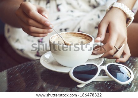 Young woman in retro dress sitting alone in cafe and shaking her cappuccino. Vintage style