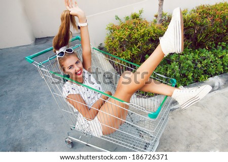 Happy screaming and laughing blonde girl sitting at shopping trolley and having fun. Pin up retro style.