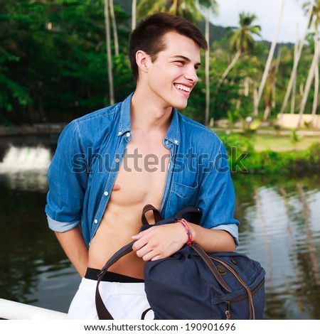 Close Up fashion portrait of young handsome man posing near lake in tropical country smiling laughing and having fun.