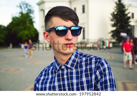Close up fashion portrait of young handsome man posing outdoor in walking street of old city wearing stylish blue mirrored sunglasses and hipster haircut.