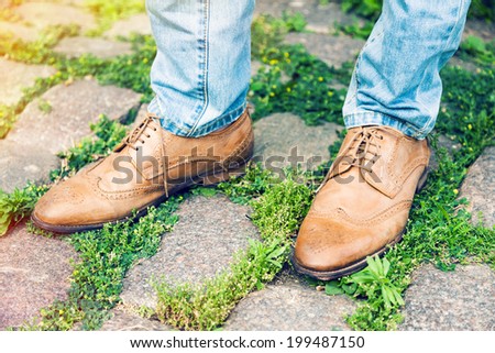 Close up fashion image of man wearing stylish retro shoes, posing outdoor in old city park.