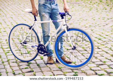 Young handsome stylish hipster man posing on the old town street with modern blue bike. Bright colors.