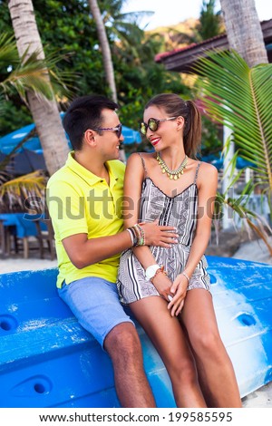Outdoor fashion portrait of young couple in love sitting on kayak boats, in exotic hot tropical country, speaking to each other joking and enjoy traveling together.
