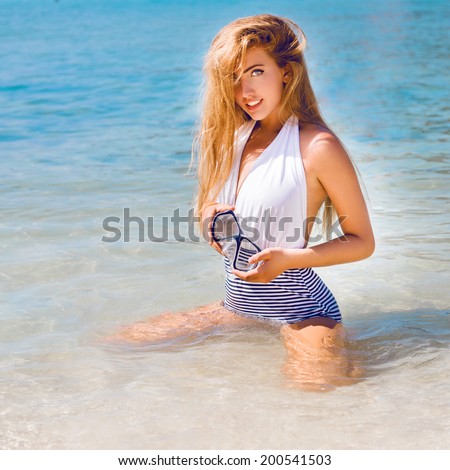 Young sexy blonde sitting in ocean clear blue water, in stylish bikini wiith mask for snorkeling, enjoy her summer vacation in hot tropical country.