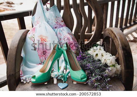 Cute woman summer floral dress green, high heels pumps , fashion blue heart necklace and flowers laying in old wooden chair. Romantic retro composition, pastel colors.