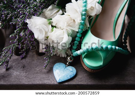 Vintage style composition of fashion green woman shoes, beautiful flowers and blue necklace with heart. Laying on old grey wooden floor.