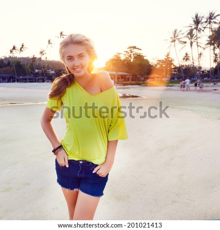 Young pretty happy blonde smiling and looking on camera, posing at californian beach at sunset.