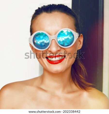Young happy tan smiling girl posing in big round stylish blue mirrored sunglasses, have big smile bright red lipstick and ponytail hairstyle.