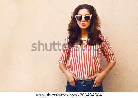 Fashion portrait of pretty brunette posing near wall, wearing bright vintage clothes sunglasses and hairstyle, soft colors.