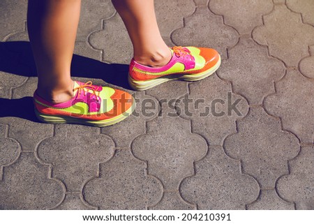 Close up outdoor fashion image of woman walking alone at the street at neon hipster sneakers, height vintage colors.