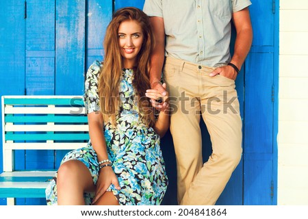 Outdoor fashion portrait of young couple in love posing at blue chubby chick beach cafe, holding hands end enjoy time together.