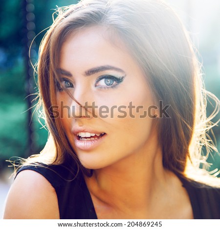 Sexy sensual woman posing with big eyes and full lips at evening sunlight at city park, having bright creative cat eye make up look.
