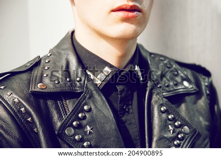 Close up fashion image of man posing in brutal leather stylish jacket wight spikes neat grunge wall.