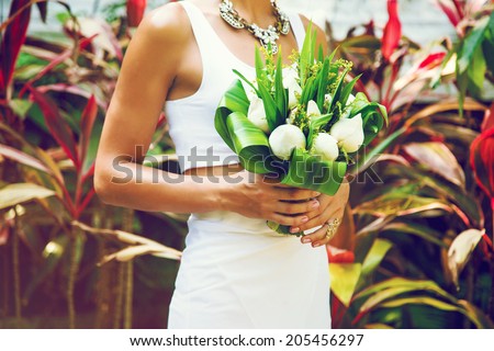 Slim tan woman holding beautiful exotic wedding bouquet with white lotus flowers, posing at park with exotic plans in Thailand.