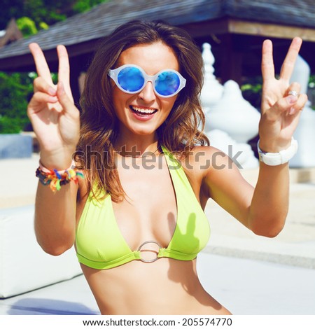 Happy young brunette smiling and getting fun in beach at hot sunny summer day, show peace science and laughing, wearing bright bikini sunglasses and accessorizes .