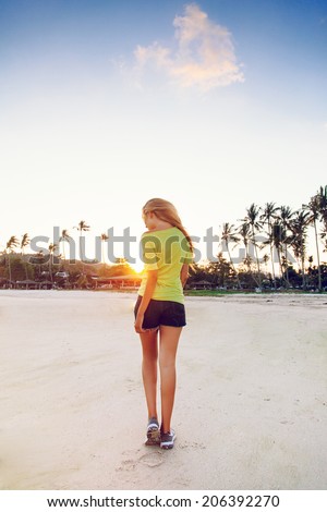 Young pretty teen tan blonde girl posing at sunset in California,beautiful view on palm trees and beach.