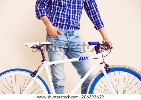 Close up fashion image of stylish guy in navy plaid shirt and vintage beans posing near beige background with his fix bike, not isolated.