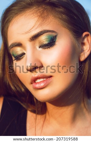 Close up outdoor fashion portrait of sensual beautiful model with perfect bronze skin, full sexy lips and bright creative green make up.