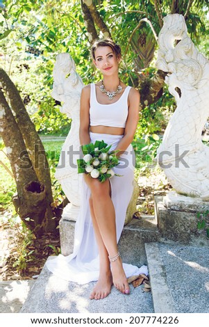 Fashion portrait of young pretty bride at creative exotic wedding at hot tropical country, posing at stylish dress with lotus bouquet.