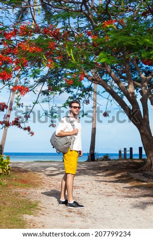 Young handsome man traveling alone with back pack, spend time at beautiful laguna surfers beach in Thailand. Nice sunny day relaxed atmosphere.