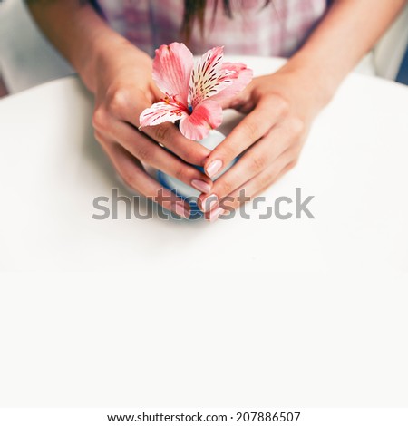 Woman holding small vase with flower in her hands, big white table, vintage toned instagram colors.