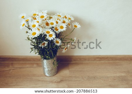 Vintage styled simple bouquet of white chamomile flowers, stain at silver vase in wooden floor. retro Instagram colors.