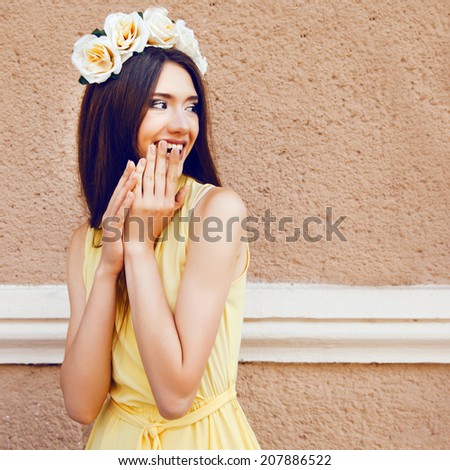 Fashion portrait of happy playful pretty brunette girl smiling and having fun, wearing pastel yellow dress and roses wreath.