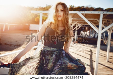 Outdoor fashion portrait of sexy beautiful blonde model posing at sunset at stylish maxi dress, warm sunny colors.